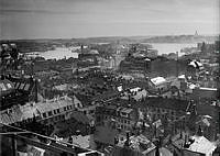 Vy söderut från södra Kungstornet över tak och takåsar på Norrmalm. I fonden Djurgården,  Skeppsholmen, Södermalm och Gamla stan.