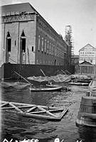 Stadshuset byggs. Fasaden åt nordost under arbete på norra trapptornet. Fiskare på håvbåtar med stora fiskhåvar fiskar på strömmen.