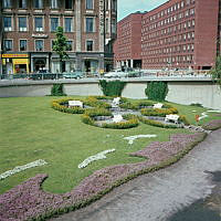 Kungsbroplan; liten park med blomformad plantering o.a. blomsterarrangemang. Vy mot kv. Härolden och Klamparen.