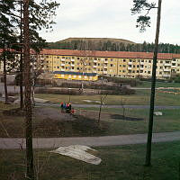 Hässelby Gård. Gårdssidan av Liljeörnsgatan 37-43 sedd från en skogsslänt vid Viveka Trolles Gränd 12. En samling barn i förgrunden. I fonden Johannelundstoppen.