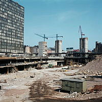 Utgrävd grop med barack, byggmaterial och bråte på platsen för nuv. Sergels Torg. Vy mot femte Hötorgshuset och bankbygge i kv. Hästskon.