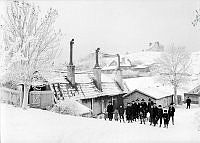 Vinterbild från Vita Bergen norrut. Vuxna och barn med kälke vid Lilla Mejtens Gränd 4. På berget i fonden byggdes Sofia kyrka 1903-1906.