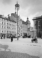 Gustav Adolfs Torg mot Arsenalsgatan med Jakobs kyrka i fonden. En man med dragkärra passerar torget. Operan stod klar 1898.