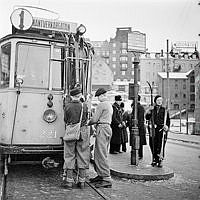 Spårvagn med skidställ på framrutan vid Slussen. Konduktör pojkar med skidor och en kvinna med skidor. I fonden Stomatol-skylten Klevgränd 1B.