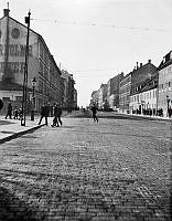 En grupp män passerar Hornsgatan vid hörnet av Rosenlundsgatan. T.v. Hornsgatan 59-61. T.h. Hornsgatan 84 västerut.