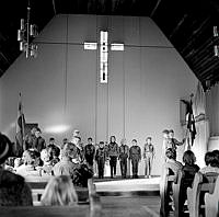 Scoutceremoni i Missionskyrkan i Enskede. Grupp av scouter och ledare flankerade av fanbärare.