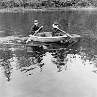 Bengt Eckerrot och Mats Lindgren och  paddlar en liten jolle. Mats Lindgren har en flytring runt halsen.