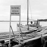 Skuta  förtöjd vid fallfärdig brygga med varningsskylt. I Stockholms norra skärgård.