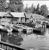 Fiskeläge i Rävsnäs med bryggor och sjöbodar. Scouter med packning på brygga.