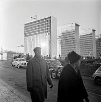 Femte hötorgshuset under färdigställande. Hamngatan mot nuvarande Sergels Torg, där byggnadsarbete pågår. Människor står vid ett plank och tittar ned i gropen.