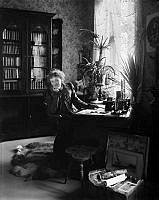 Porträtt av författarinnan Alfhild Agrell. Interiör med skrivbord och bokskåp.