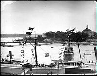 Flaggspel på båtar vid Skeppsbrokajen med anledning av Kejsar Vilhelm II:s besök. I bakgrunden Skeppsholmen.