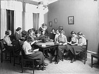 Unga kvinnor som sitter runt ett bord och läser. Gustaf Vasa församlings ungdomsklubb.