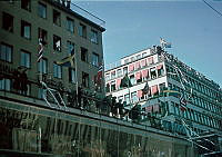 Glada människor firar fredsdagen den 7 maj 1945 längs Kungsgatan 44-46 med hissade flaggor, serpentiner och konfetti.