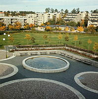 Vällingby; parkområde med liten damm, parkbänkar och cirkelformad stenläggning belägen väster om Solursgången. Vy åt norr.