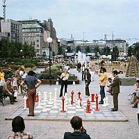 Schackspelare i Kungsträdgården. Bräde av olikfärgade betongplattor lagda på marken med knähöga träpjäser. Vy mot parkens norra del.