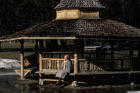 Lill-Jansskogen. Ugglevikskällans paviljong. Äldre kvinna som sitter och solar vid paviljongen.