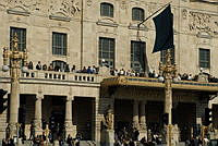 Parti av Dramatiska Teaterns fasad mot Nybroplan. Mycket folk på teaterns trappa och balkong.