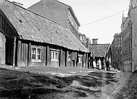 Tegnérgatan mot öster från Återvändsgränd. (Tegnérgatan hette Trebackarlånggatan före 1885). Några personer står vid trähusen.