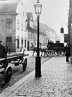 Regeringsgatan 54 A, B och C söderut från hörnet av Lästmakargatan. Ett hästfordon, två hästar och en vagn med texten Nynäs Limpor, passerar gatukorsningen.