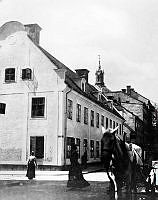 Några kvinnor och en häst passerar Storgatan 12 vid hörnet av Skeppargatan (t.v.). Hedvig Eleonora kyrkas torn i fonden.