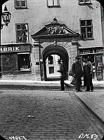 Några män står i hörnet av Mariagränd och Götgatan. I bakgrunden ligger portalen till Götgatan 16, Ebba Brahes palats.
