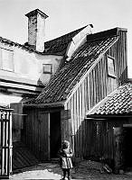 Ett barn står på gårdssidan av Västra Kvarngränd 6 och 8. Nuv. kv. Kvadraten ung. norr om Allhelgonagatan, tidigare Gotlandsgatan.