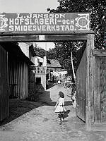 En liten flicka står i portöppningen till gården vid Nytorget 37. Här finns L. Janssons hovslageri och smidesverkstad. Nuv. Nytorget 3.