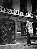 En kvinna passerar porten vid Högbergsgatan 30 A. Firman Beskow & Co, gas och vattenledningar, har skyltar på fasaden.