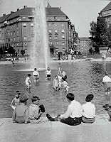 Barnen leker i dammen framför fontänen vid Karlaplan. I bakgrunden ligger Karlaplan 9.