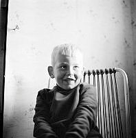 Porträtt av pojken Thomas Risberg på en stol mot bakgrund av blommig tapet i Rävsnäs på Rådmansö.