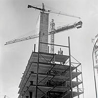 Femte hötorgshuset under uppförande. Två arbetare står högt upp på balkkonstruktionen.