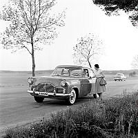 Ford Zephyr parkerad vid kanten på en landsväg. En kvinna står och samtalar med föraren.