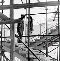 Två byggnadsarbetare i en byggnadsställning med trappor.