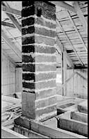 Interiör visande takkonstruktion, skorsten med isolering av eternitplattor mot trä och övre bjälklaget i husbygge i Ängbys småstugeområde