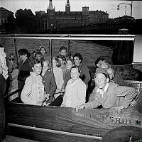 Skånska barn besöker Stockholm. Grupporträtt i en båt. Vy mot Norstedts förlag/Riddarholmen.