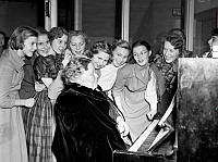 Timmermansgatan 21. Julfest på Södermalms kommunala flickskola. Ungdomar och en äldre dam samlade runt ett piano.