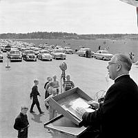Skarpnäcks flygfält. Biskop Odd Hagen predikar på Sveriges första drive-in-gudstjänst. Tusen bilar stod tätt uppställda och ca sextusen personer deltog. Altaret var rest på ett lastbilsflak.