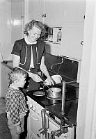 Österskär, Roslagen. Köksinteriör med en kvinna som lagar mat och en pojke som tittar på.