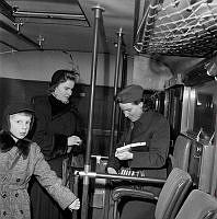 Interiör från en buss med passagerare och en konduktör.