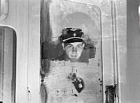 Porträtt av en okänd man i skärmmössa från Stockholms Spårvägar, förmodligen en konduktör, som tittar ut igenom en spårvagns isiga fönster.