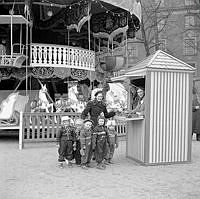 Kungsträdgården. Tivoli/karusell i samband med Röda Korset-veckan. En kvinna med en grupp barn vid biljettkassan.