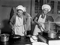 Folkskola på Lidingö. Pojkar lär sig laga mat, baka och hushållsskötsel. Porträtt av två pojkar i förkläden och kockmössa.