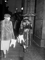 Kunglig kortege. Gustaf VI Adolf fyllde 70 år och red kortege genom staden. Längs kortegens väg stod stockholmare och väntade i regnet. Två kvinnor på väg hem bärandes på varsin pall.