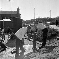 Klara Mälarstrand. Värmebölja i staden. Två män dricker vatten från en pump.