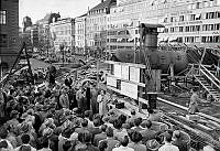 Vid Vasagatan står tunnelbanebyggets arbetschef Gunnar Hult med en pekpinne och demonstrerar den första färdiga kasunen vid Centralen. Åhörarna är en stor grupp män från Teknologföreningen.