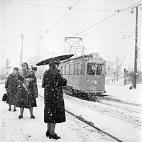 Vinterbild. Snöig gatumiljö där spårvagnslinje 9 tar sig fram.