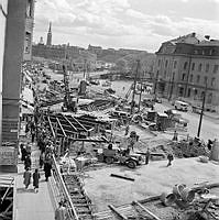 Vasagatan. Vy mot Tegelbacken och Riddarholmen. T.v. pågår arbete med att däcka över tunnelschaktet för tunnelbanan. T.h. Centralstationen.