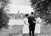 Skeppsholmen utanför Skeppsholmskyrkan med utsikt mot Skeppsbron. Amiralitetspastor G.A Brandt med två av sina konfirmander, Margareta Olofsson och Barbro Dölling, i samband med konfirmation i kyrkan.