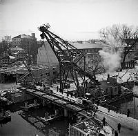 Reimersholme. Nya bron till Reimersholme, Reimersholmsbron. Betongbron över Bergsundet byggdes i två omgångar, här läggs den andra brohalvans järnkonstruktion på plats med hjälp av en pontonkran.